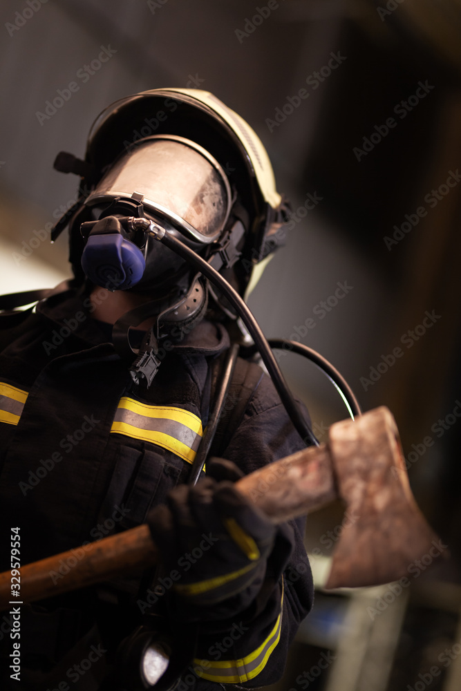 female firefighter portrait wearing full equipment, oxygen mask, and an axe. smoke and fire trucks in the background.