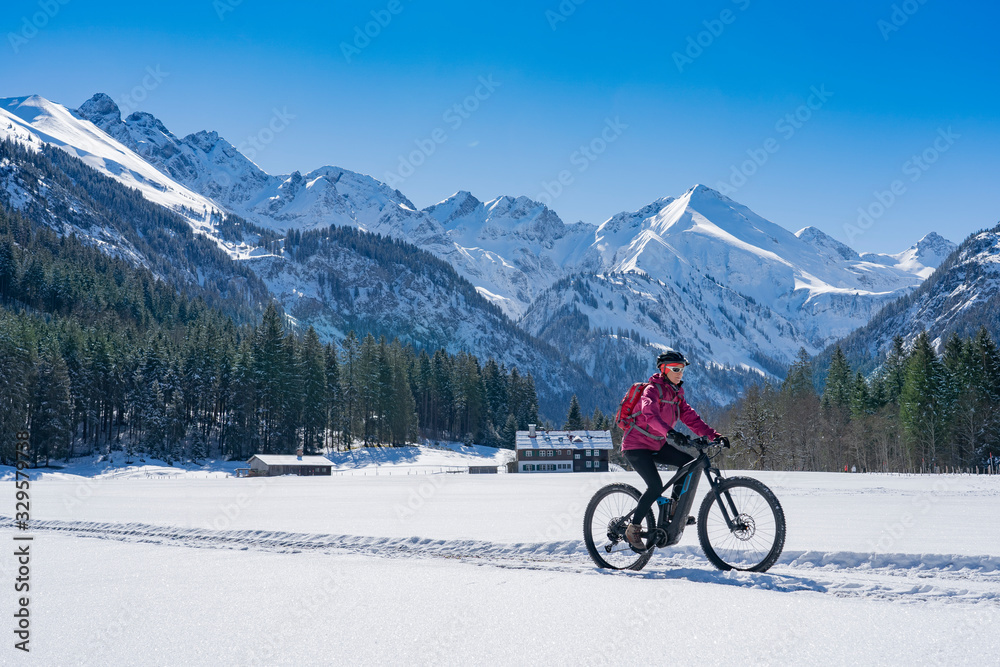 nice senior woman riding her electric mountainbike on a sunny winter day in the Allgau alps near Oberstdorf, Bavaria, Germany