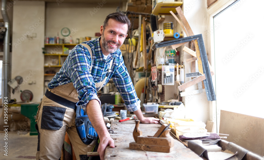Smiling and proud mature carpenter in his carpentry workshop Smiling and proud mature carpenter in his carpentry workshop