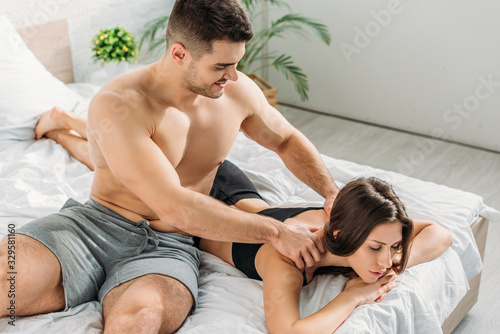 sexy shirtless man making shoulders erotic massage to attractive girlfriend lying with closed eyes photo