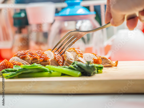 Closeup of sliced roasted duck, green vegatable, fork on wooden cutting board and woman 's hand with blurry kitchen background.