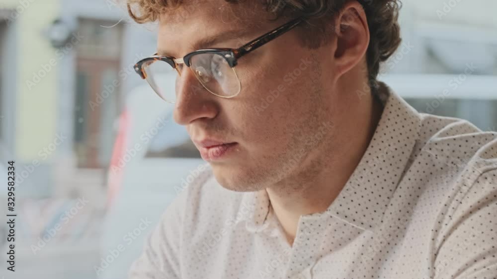 A focused young man wearing casual clothes is using his smartphone in the white cafe A focused young man wearing casual clothes is using his smartphone in the white cafe