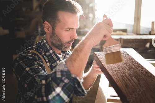 Craftsman painting a wooden board by paintbrush in his carpentry workshop