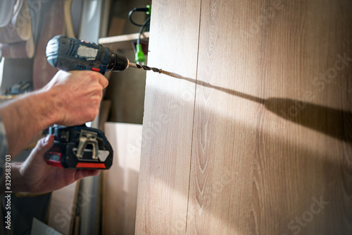 Craftsman drilling a hole by drill in a wooden board