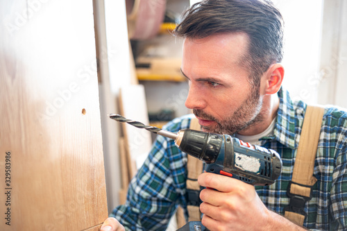 Craftsman drilling a hole by drill in a wooden board