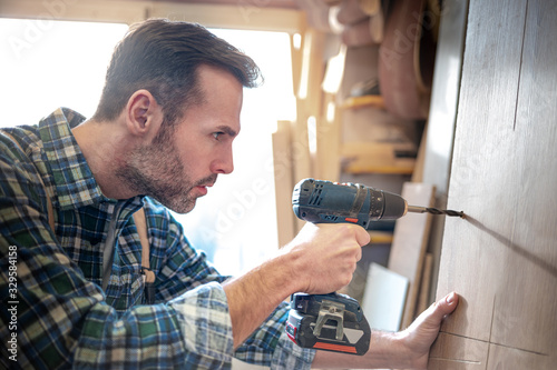 Craftsman drilling a hole by drill in a wooden board