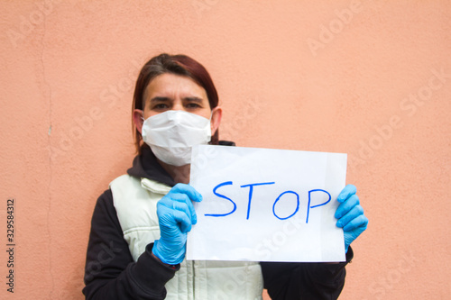 woman with white sign indicating stop wearing white health mask and blue doctors gloves defying the virus type coronavirus or covid 19 photo