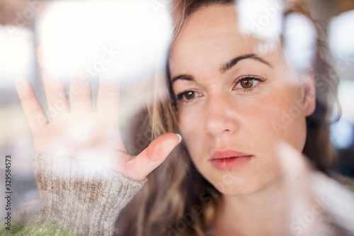 Young sad and depressed woman indoors by window at home.
