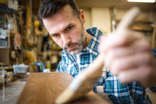 Craftsman applies varnish on wooden board by paintbrush in his carpentry work...