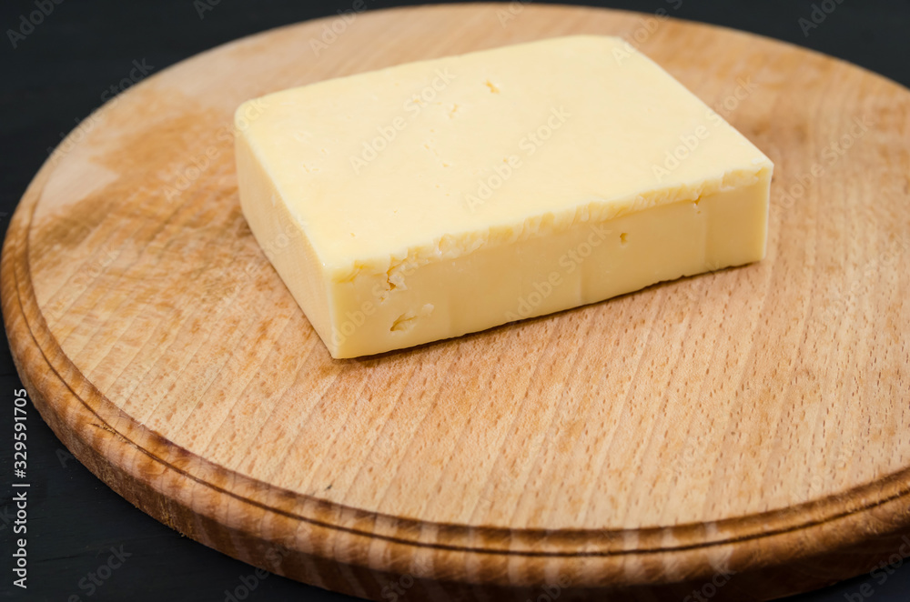 piece of hard cheese on a wooden board. Black background.