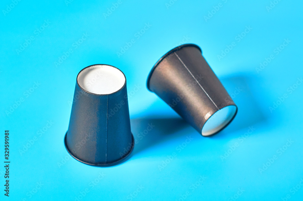 Two empty black cardboard glasses for hot beverages on blue background. Concept of environmental protection, coffee break, ecology, garbage recycle Two empty black cardboard glasses for hot beverages on blue background. Concept of environmental protection, coffee break, ecology, garbage recycle
