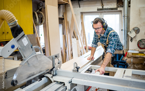 Carpenter using circular saw to cut a large wooden board at carpentry workshop