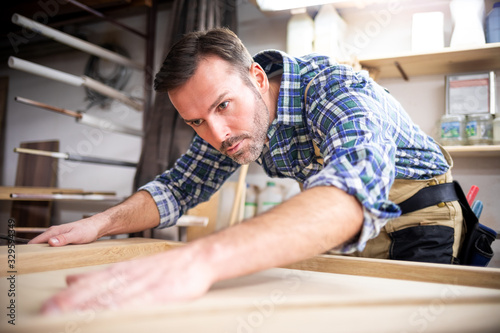 Carpenter looking at polished wood after sanding in his carpentry workshop