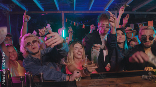 Photography Attractive modern youth waving dollar banknotes on bar counter waiting for their order cocktail drinks while partying in the nightclub