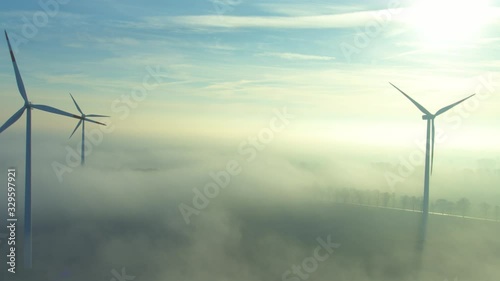 Camera flying along rotating wind wheels in backlit with ground fog(aerial view)