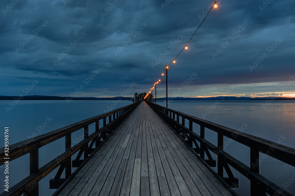 Long wooden pier over a lake at night with lights strung overhead. Sweden.