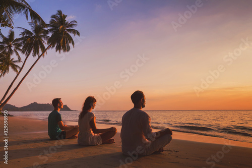 yoga retreat on the beach at sunset, silhouettes of group of people meditating photo