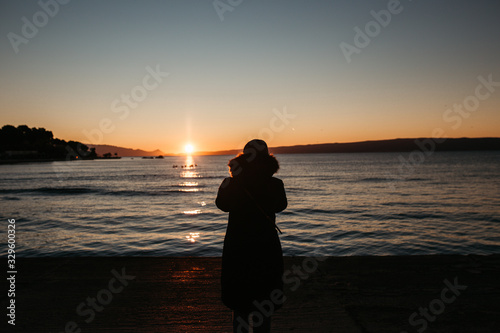 photo of young European Muslim women with hijab standing and looking into sea. She is standing turned back with her hands in the air. She is happy and relaxed. Photos taken during sunrise. 