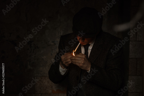 A man smokes a cigarette in the image of an English retro gangster in Peaky blinders style. photo