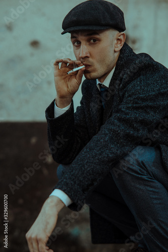 A man smokes a cigarette in the image of an English retro gangster in Peaky blinders style.