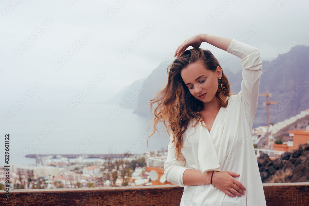 Woman on a background of mountains and a city. Girl travels in Tenerife. The girl in the summer knows the world. Great traveling, happy with long hair. Summer.