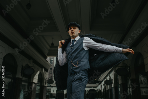 A man posing in the image of an English retro gangster in Peaky blinders style at city street. photo