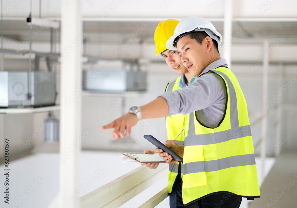 Two engineers man standing in the site. Engineer holding tablet and point to machine and explain detail of machine to other engineer. Engineering and construction concept. Two engineers man standing in the site. Engineer holding tablet and point to machine and explain detail of machine to other engineer. Engineering and construction concept.