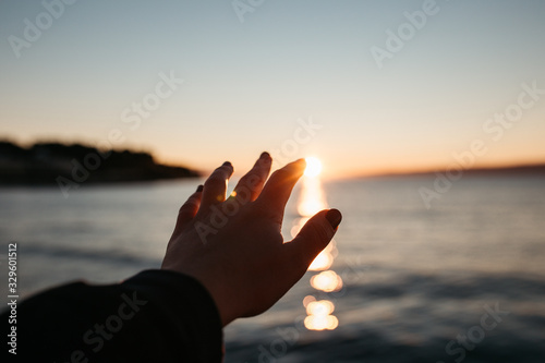 Close up photo of female hands trying to reach sun above sea,  during sunrise.  © Melika