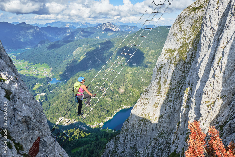 Woman on via ferrata ladder above Gosau lake, on the Intersport Klettersteig Donnerkogel route, in Austria. High angle view on a Summer day.