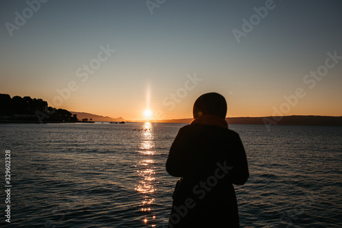 photo of young European Muslim women with hijab standing and looking into distance. Sea is in the background. She is happy and relaxed. Photos taken during sunrise. 
