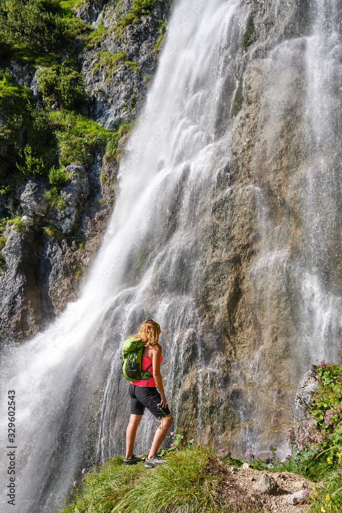 Woman hiker, with a green backpack, looks up at Dalfazer waterfall, Austria.