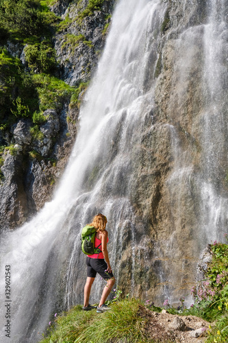 Woman hiker, with a green backpack, looks up at Dalfazer waterfall, Austria.