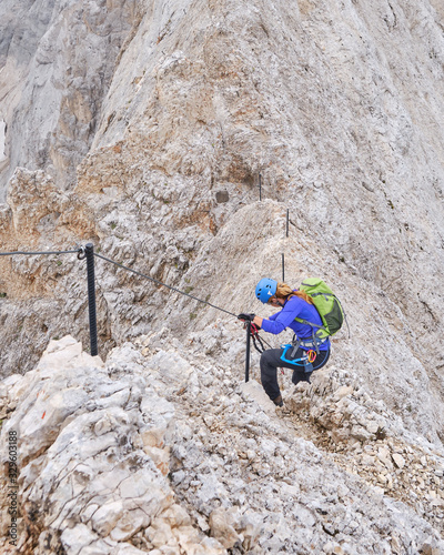 Woman descending a ridge section on via ferrata Eterna Brigata Cadore towards Punta Serauta on Marmolada glacier, with clouds rolling in. photo