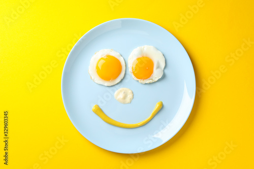 Smile face made of plate with fried eggs on yellow background, top view