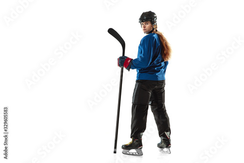 Young female hockey player with the stick on ice court and white background. Sportswoman wearing equipment and helmet posing. Concept of sport, healthy lifestyle, motion, action, human emotions.