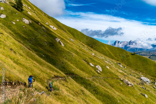 Zwei Mountainbiker auf einem Singletrail über eine Wiese in den Dolomiten photo