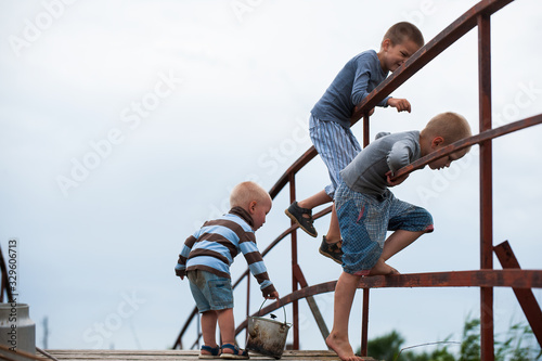 Funny children in bright clothes took fishing rod and tried to fish on bridge over river. Funny situations while fishing. Summer vacation in village. Brothers are happy together