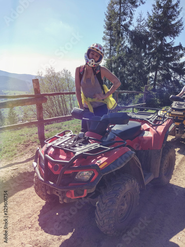 Young woman in a helmet on a quad bike on the background of the forest and the fence