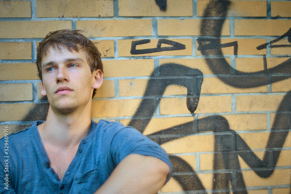 custom made wallpaper toronto digitalReminiscing young man sitting and leaning by an urban brick wall wearing a blue shirt in summer.