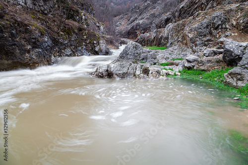 Powerful, blurred motion, colorful water of a mountain creek after rain cascading through the narrow, rocky canyon photo