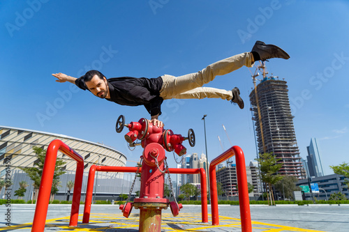 Photography Flexible Acrobat keep balance with one hand on the fireman hydrant with blurred Dubai cityscape