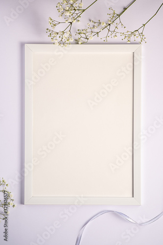 White picture frame with empty template, gypsophila flowers and fabric ribbon, white background, mockup card