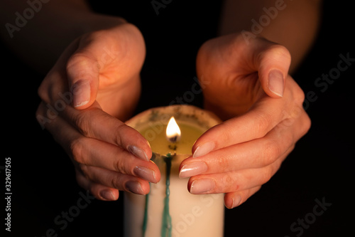 Women's hands above the burning candle close-up. Magic fire, the witch predicts. Isolate on a black background, a static shot