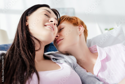 Same sex couple smiling with closed eyes on bed