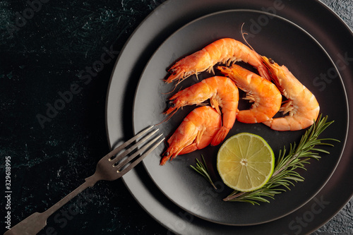 Boiled shrimps with rosemary and lime on a black plate.
