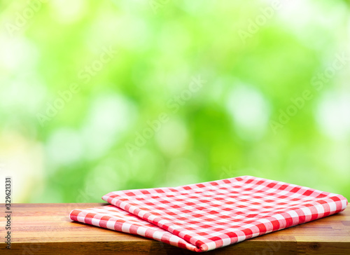 Red checked tablecloth on wood with blur green bokeh of tree background.Summer and picnic concepts