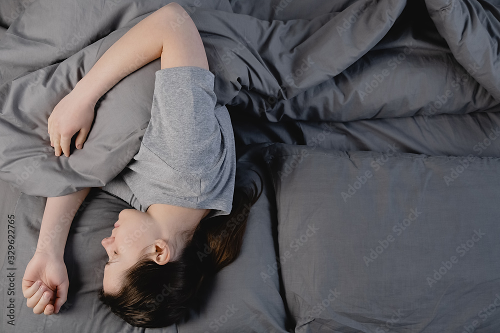 Top view of serene calm brunette woman sleeping in comfortable bed lying on soft pillow orthopedic mattress, peaceful young girl resting covered with blanket on grey sheets in bedroom. Top view of serene calm brunette woman sleeping in comfortable bed lying on soft pillow orthopedic mattress, peaceful young girl resting covered with blanket on grey sheets in bedroom.