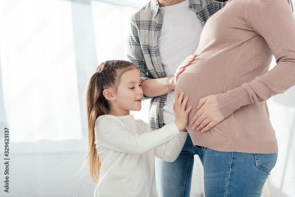 Child and parent touching belly of pregnant mother in living room Child and parent touching belly of pregnant mother in living room