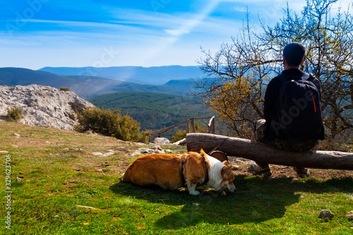Tourist sitting on a bench and looking at the mountains with his dog - funny Welsh Corgy