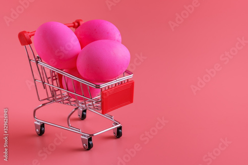 Trolley Shopping cart with Easter eggs on pink background.